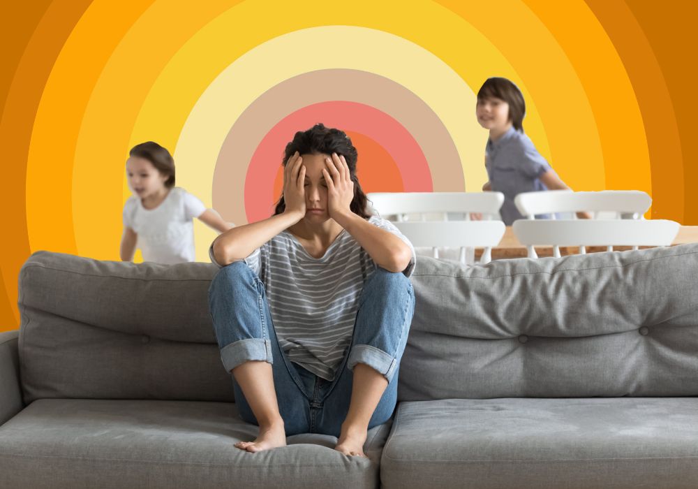 Image of a stressed mum sitting on the sofa with her feral kids running around in the background while she wishes she could run away to a cabin in the woods to live as a crazy old lady wrapped in blankets and covered in twigs where all she had to concern herself with was writing stories and drinking eta