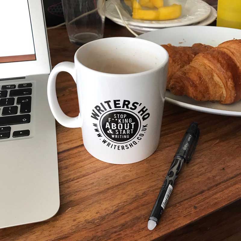 A WHQ stop fucking about mug next to a laptop and croissants at a writers' retreat