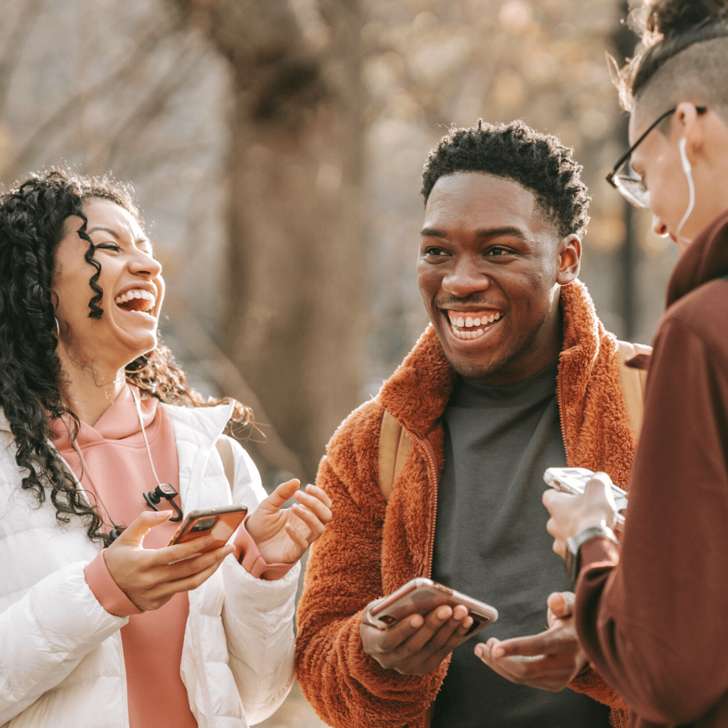 Thre people holding their phones and laughing together.