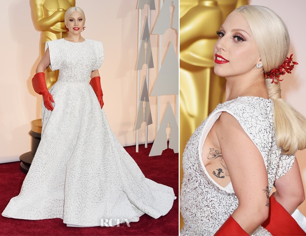 Image of Lady Gaga on the red carpet at the 2015 Oscars wearing a white embroidered dress with swept back blonde hair and bright red rubber gloves.