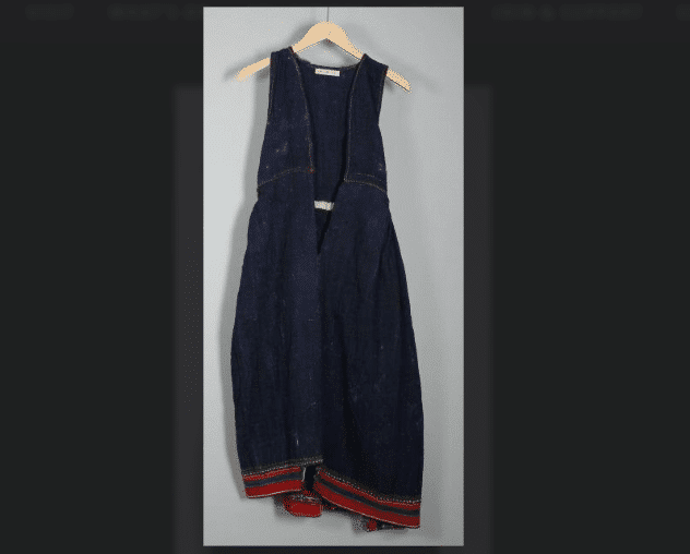 A photograph of a dark-coloured sleevelss 19th century Croatian dress with a red pattern along the hem