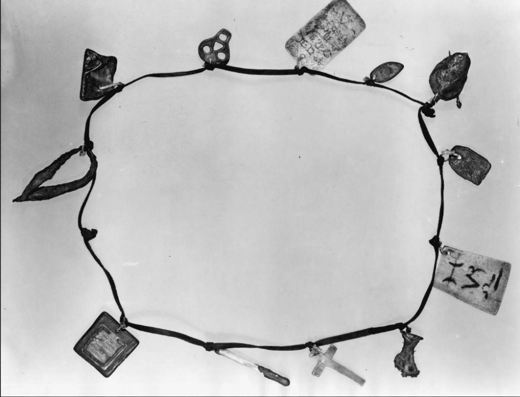 A black and white photo of a 'witch's wreath': a collection of carved stones, charms and trinkets tied onto what looks like a leather thong. 