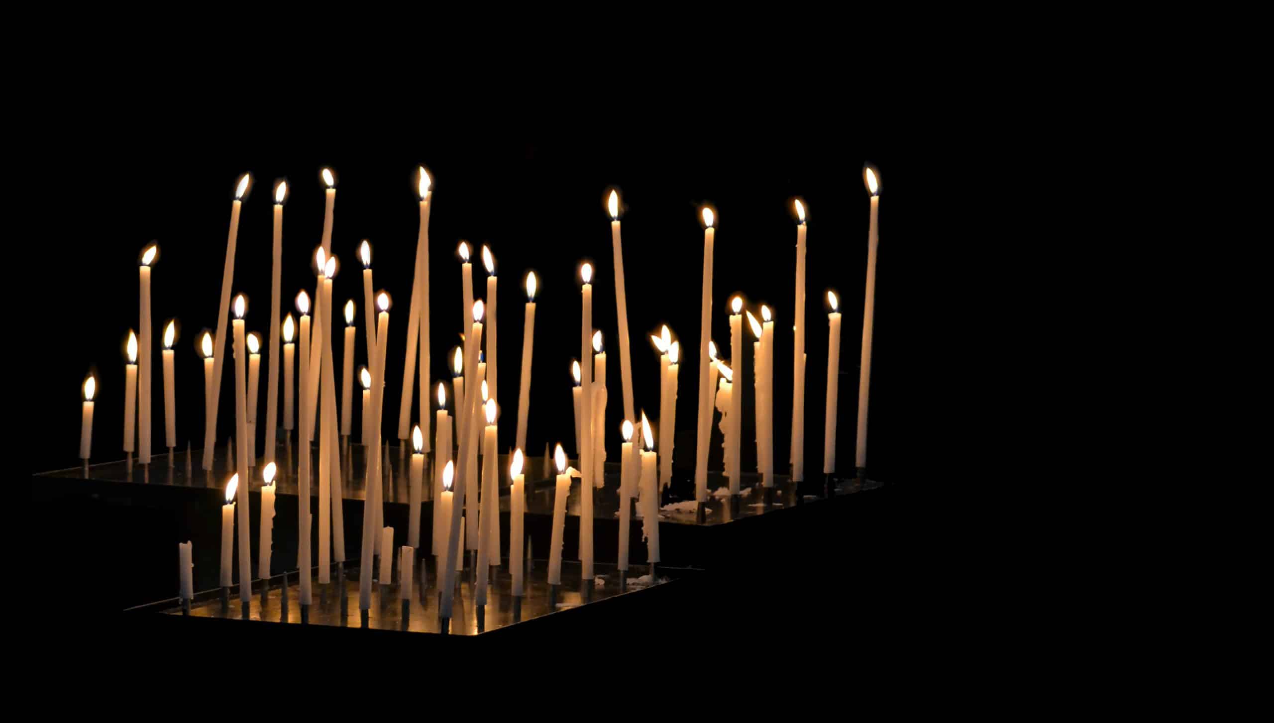 A photograph of a cluster of long, thin candles in a dark space.