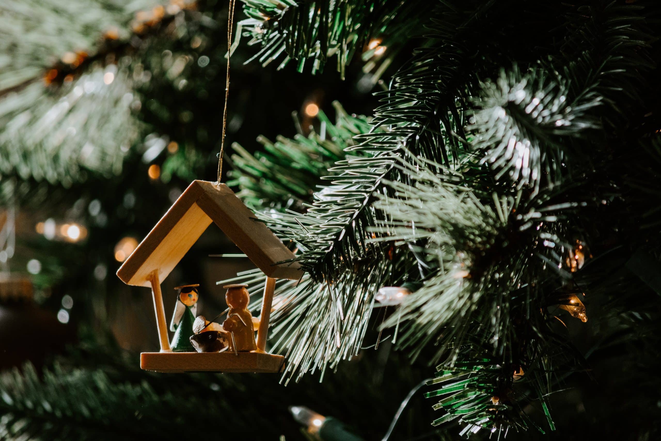 A close up photo of a Christmas tree showing a tiny wooden nativity decoration