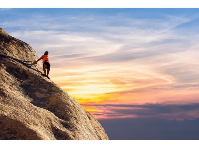 A rock climber reaching the summit with a beautiful sunrise behind them