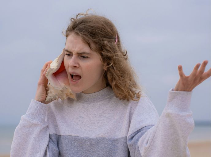 Woman on a beach shouting into a shell.