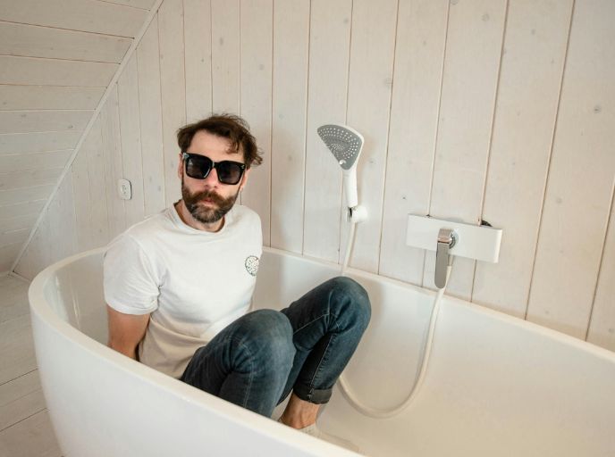 Man in white t-shirt, jeans and shades sitting in an empty bath tub