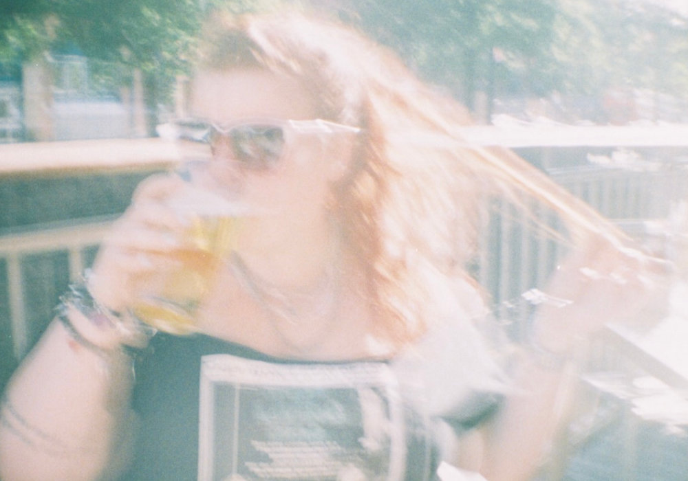 A blurry picture of Alice Slater drinking a pint of cider in a pub with the sun behind her, looking legit dreamy and magical